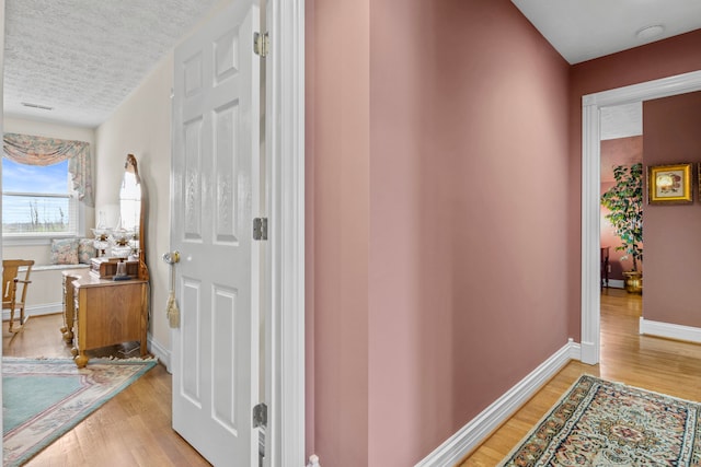 hall with a textured ceiling and light wood-type flooring