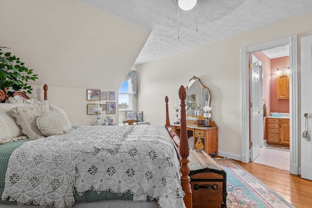 bedroom with ensuite bath, lofted ceiling, hardwood / wood-style floors, and a textured ceiling