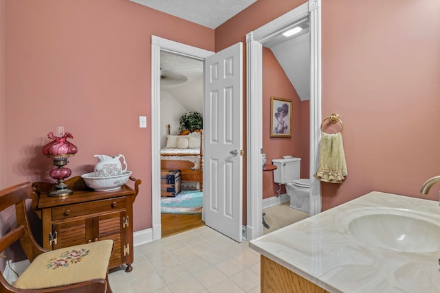 bathroom featuring lofted ceiling, vanity, a textured ceiling, tile patterned floors, and toilet