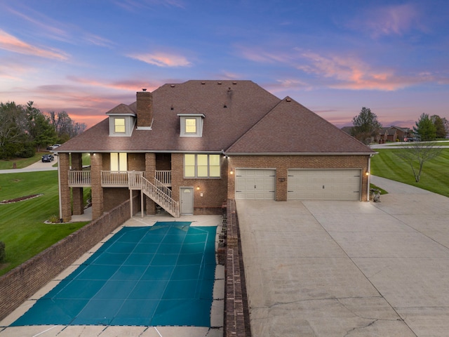 back house at dusk featuring a garage, a covered pool, and a lawn