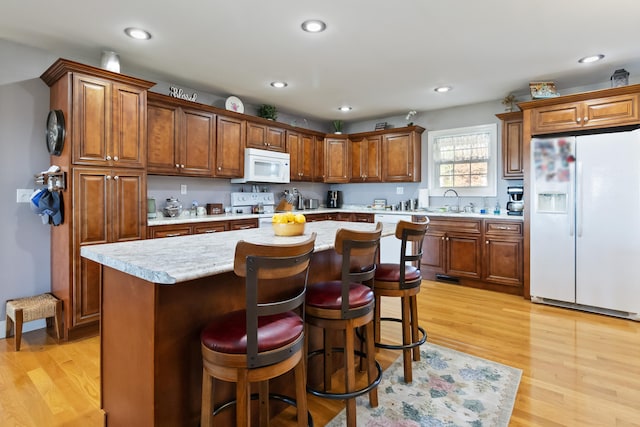 kitchen featuring white appliances, sink, light wood-type flooring, and a center island