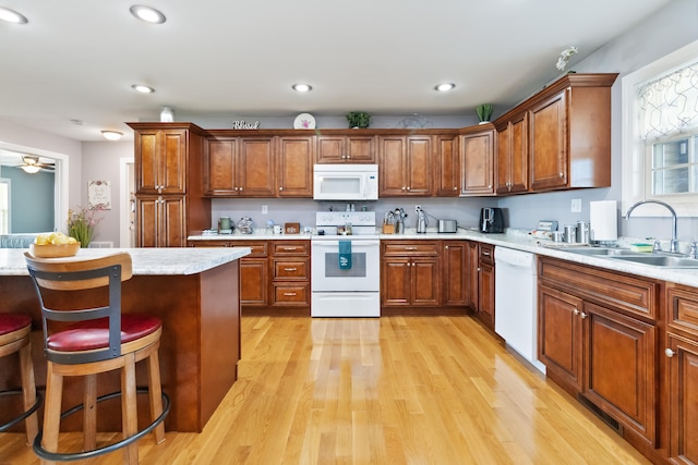 kitchen featuring sink, a breakfast bar, ceiling fan, white appliances, and light hardwood / wood-style flooring