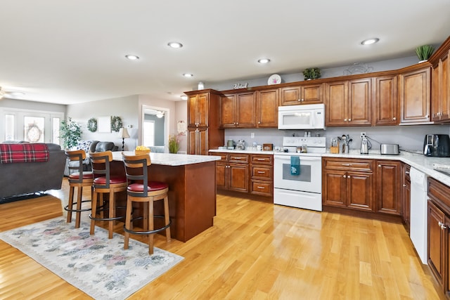 kitchen with ceiling fan, a kitchen island, a breakfast bar, light hardwood / wood-style flooring, and white appliances