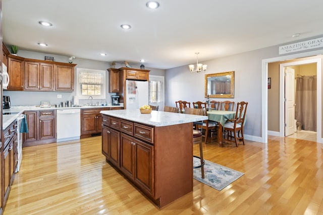 kitchen with white appliances, pendant lighting, a kitchen island, and light hardwood / wood-style flooring