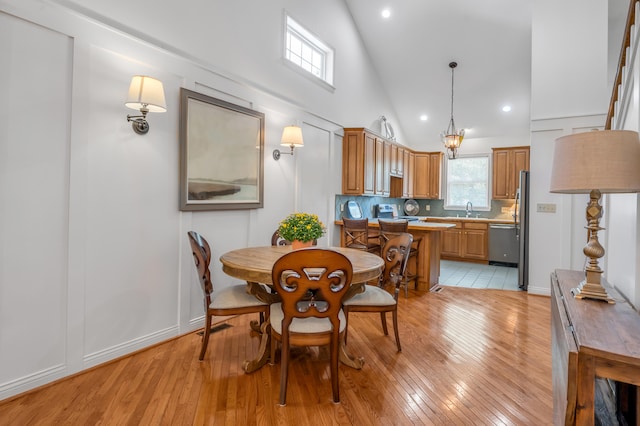 dining space with high vaulted ceiling, light hardwood / wood-style floors, sink, and a chandelier