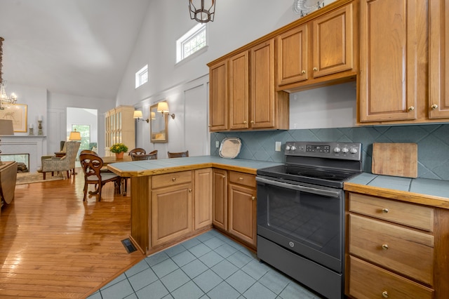 kitchen featuring tile counters, a healthy amount of sunlight, stainless steel electric range oven, and decorative light fixtures