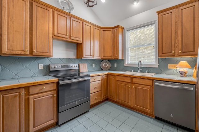 kitchen with tile countertops, sink, appliances with stainless steel finishes, vaulted ceiling, and decorative backsplash