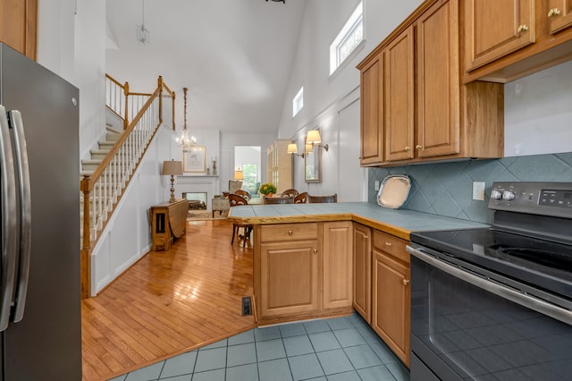 kitchen with stainless steel appliances, light wood-type flooring, high vaulted ceiling, tile counters, and kitchen peninsula