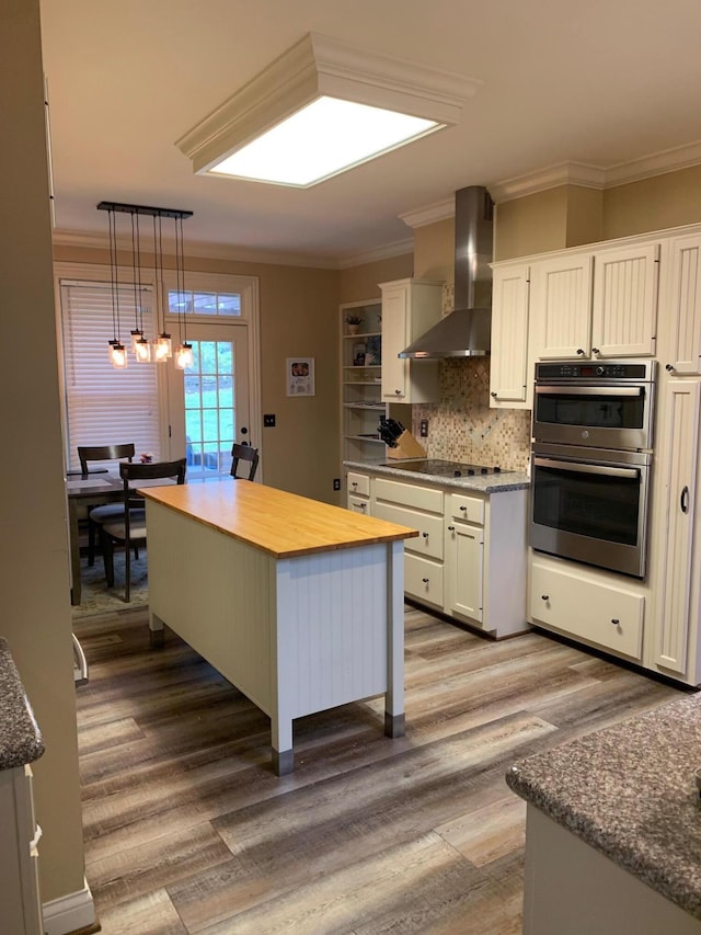 kitchen with white cabinetry, wall chimney exhaust hood, hanging light fixtures, and a kitchen island