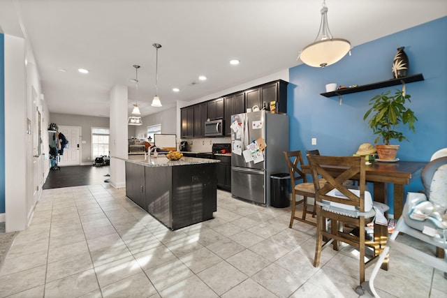 kitchen featuring stainless steel appliances, light stone counters, decorative backsplash, an island with sink, and decorative light fixtures