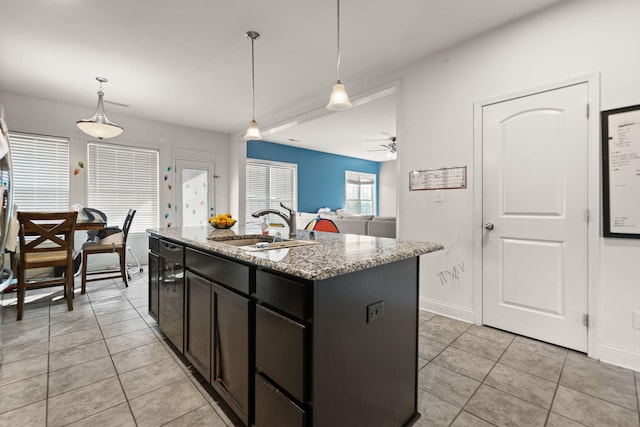 kitchen with light stone countertops, pendant lighting, sink, ceiling fan, and a kitchen island with sink