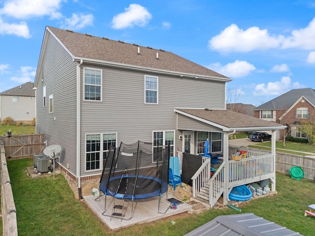 back of property featuring a lawn, a wooden deck, central AC, and a trampoline