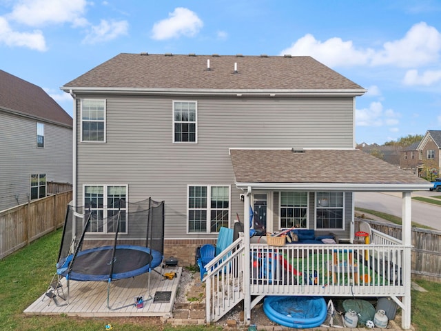 back of property with a trampoline and a deck