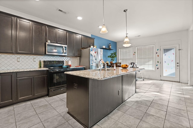 kitchen with stainless steel appliances, dark brown cabinets, hanging light fixtures, and a kitchen island with sink