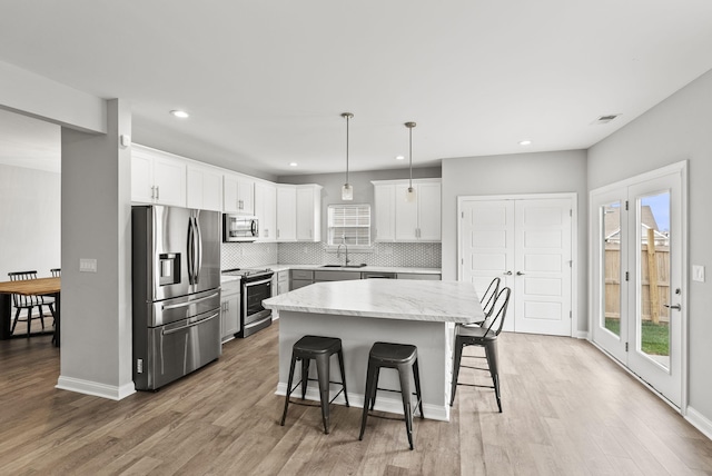 kitchen with sink, hanging light fixtures, light hardwood / wood-style floors, a kitchen island, and stainless steel appliances