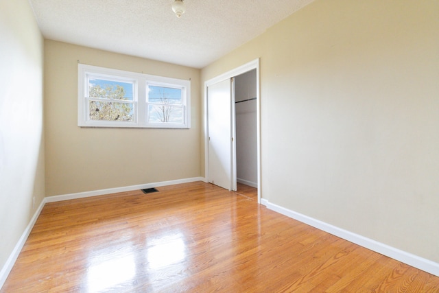 unfurnished bedroom featuring a textured ceiling, light hardwood / wood-style floors, and a closet