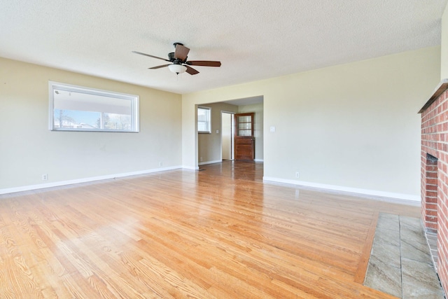 unfurnished living room featuring a fireplace, ceiling fan, a textured ceiling, and light hardwood / wood-style flooring