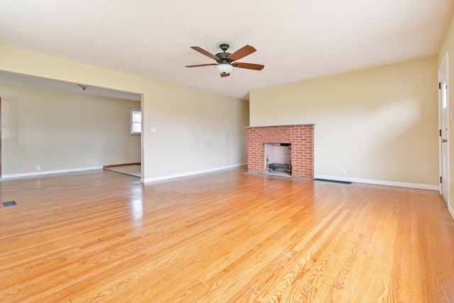 unfurnished living room featuring a brick fireplace, ceiling fan, and light wood-type flooring