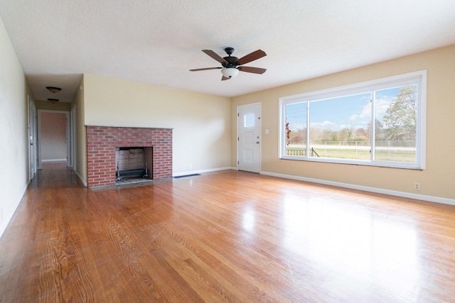 unfurnished living room with a textured ceiling, light wood-type flooring, a brick fireplace, and ceiling fan