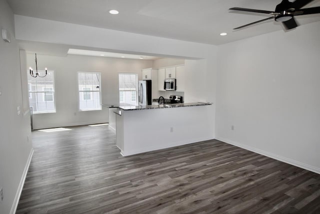 kitchen featuring kitchen peninsula, appliances with stainless steel finishes, dark stone counters, dark hardwood / wood-style floors, and white cabinetry