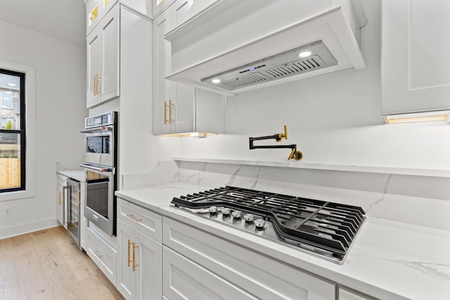 kitchen featuring premium range hood, white cabinetry, light hardwood / wood-style floors, and stainless steel appliances