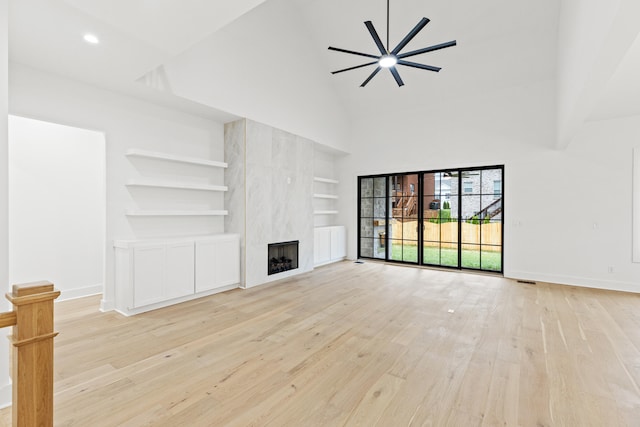 unfurnished living room with built in shelves, a large fireplace, light hardwood / wood-style floors, and ceiling fan