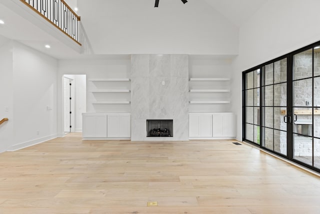 unfurnished living room featuring light hardwood / wood-style floors, a fireplace, and high vaulted ceiling