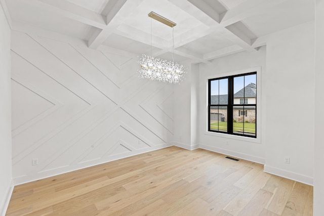 spare room featuring a notable chandelier, beamed ceiling, coffered ceiling, and light wood-type flooring