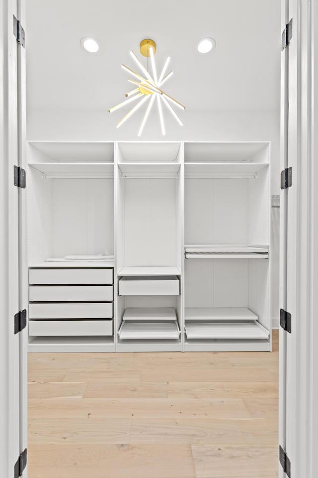 spacious closet with hardwood / wood-style flooring and a notable chandelier