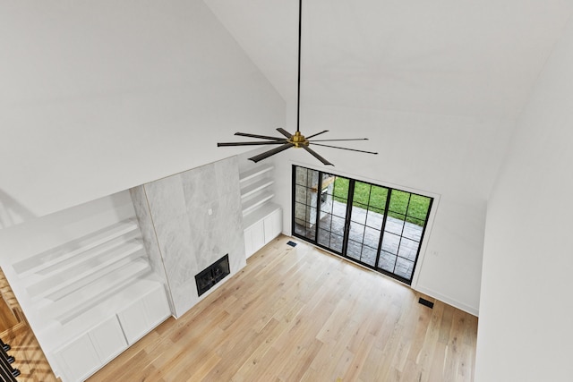 unfurnished living room with ceiling fan, light wood-type flooring, and a high ceiling