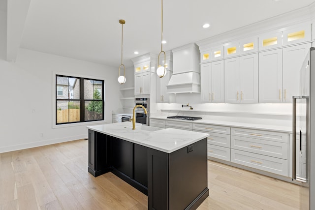 kitchen featuring sink, light hardwood / wood-style floors, decorative light fixtures, a kitchen island with sink, and white cabinets