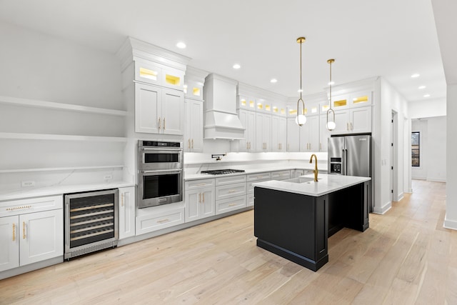 kitchen with appliances with stainless steel finishes, white cabinetry, beverage cooler, and a kitchen island with sink