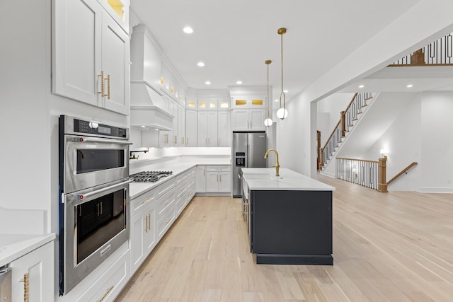 kitchen with white cabinetry, stainless steel appliances, an island with sink, pendant lighting, and light hardwood / wood-style floors