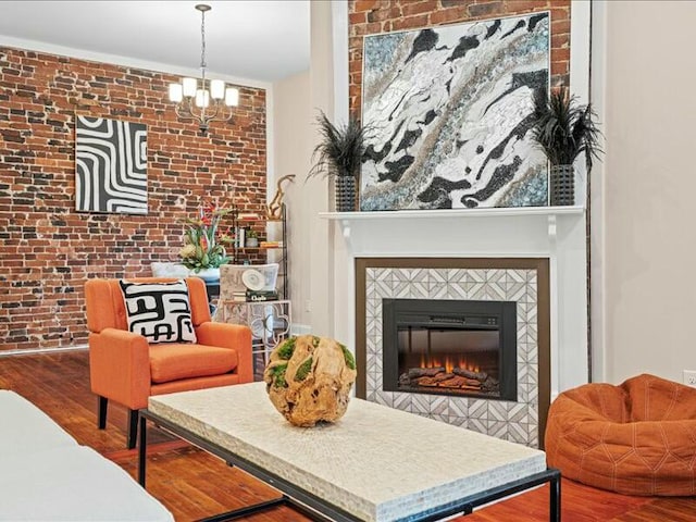 living area with hardwood / wood-style flooring, a notable chandelier, a tile fireplace, and brick wall