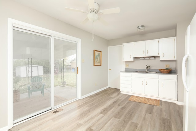 kitchen with light wood finished floors, visible vents, white cabinets, freestanding refrigerator, and a sink