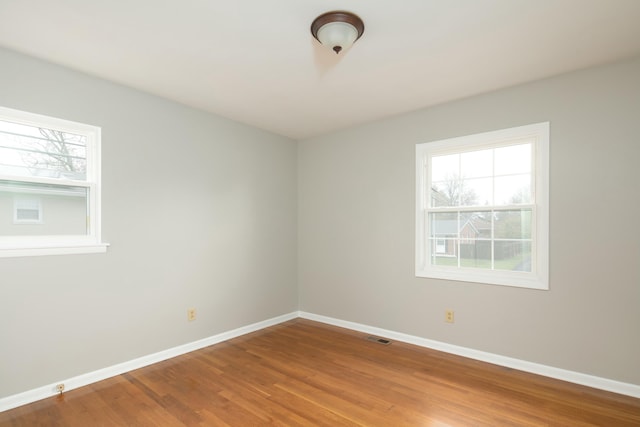 spare room with wood finished floors, visible vents, and baseboards