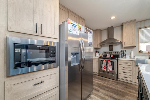 kitchen with light brown cabinetry, dark hardwood / wood-style floors, wall chimney range hood, and stainless steel appliances