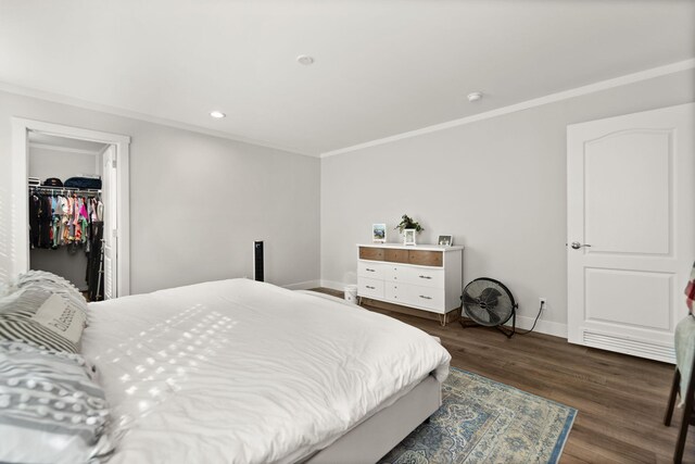 bedroom featuring a walk in closet, a closet, dark hardwood / wood-style flooring, and crown molding