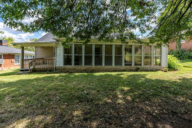 rear view of house featuring a lawn, a wooden deck, and a sunroom