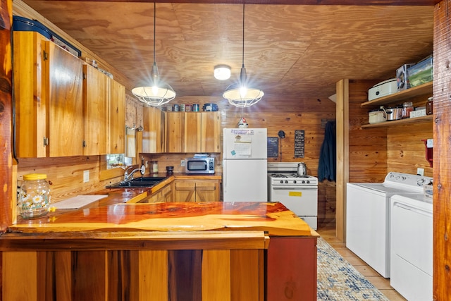 kitchen featuring sink, washing machine and dryer, wood walls, white appliances, and decorative light fixtures