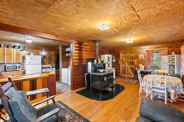 living room with independent washer and dryer, a wood stove, wooden ceiling, and light wood-type flooring