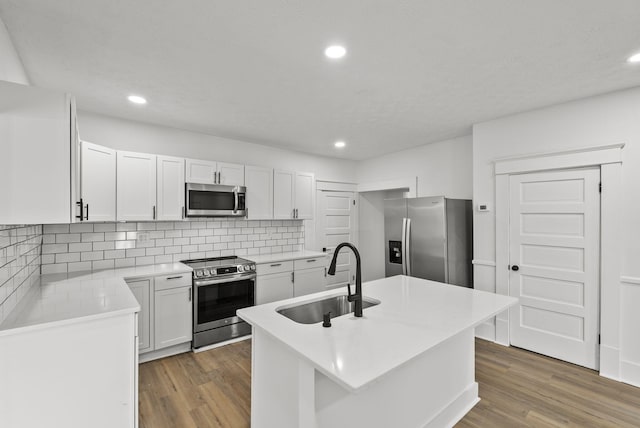 kitchen featuring appliances with stainless steel finishes, sink, wood-type flooring, white cabinets, and an island with sink