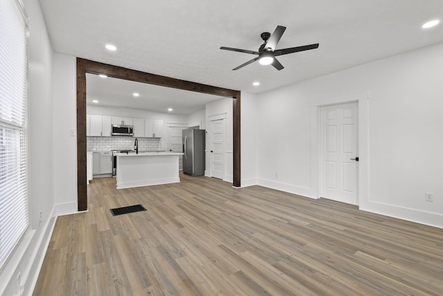 unfurnished living room with light wood-type flooring, ceiling fan, and sink