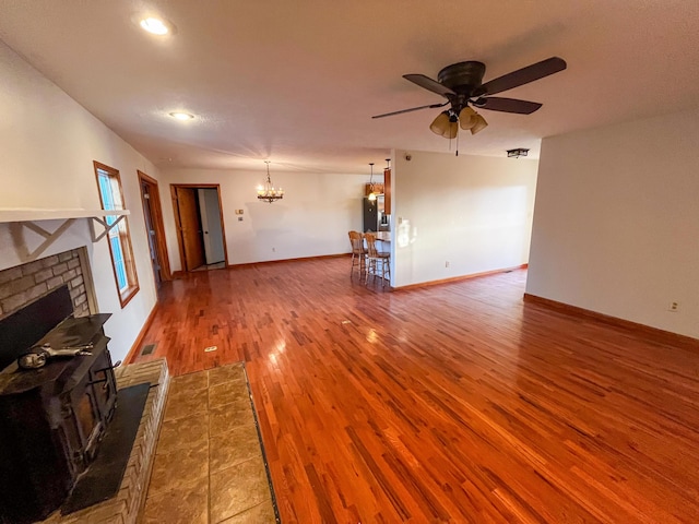 unfurnished living room with wood-type flooring, ceiling fan with notable chandelier, and a wood stove