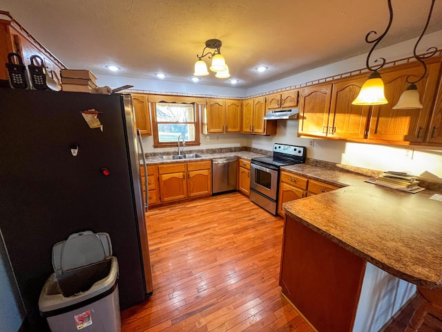 kitchen with sink, light wood-type flooring, appliances with stainless steel finishes, decorative light fixtures, and kitchen peninsula