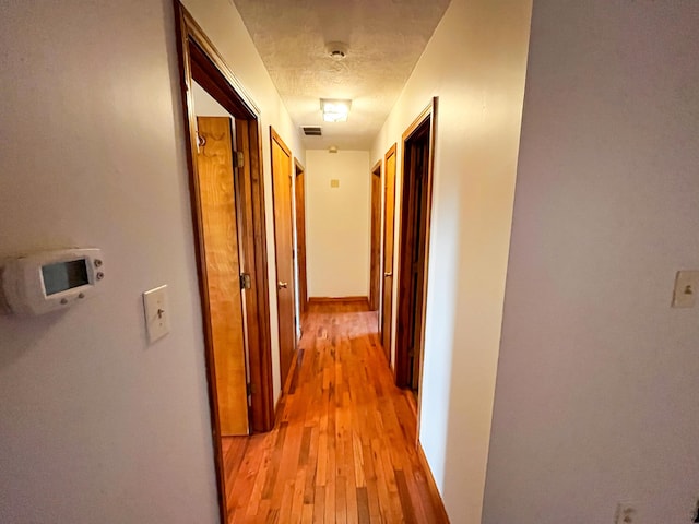 corridor with a textured ceiling and light hardwood / wood-style flooring