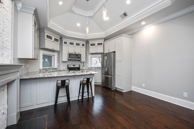 kitchen featuring visible vents, stainless steel appliances, a peninsula, a breakfast bar area, and light stone countertops