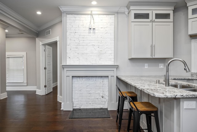 kitchen with visible vents, a kitchen bar, a sink, light stone counters, and dark wood finished floors