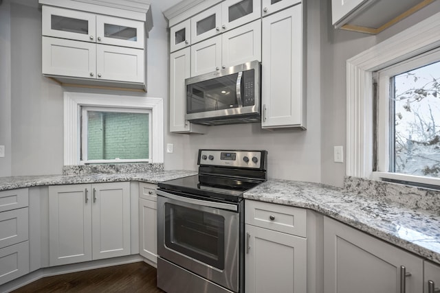 kitchen with light stone counters, glass insert cabinets, dark wood-type flooring, and appliances with stainless steel finishes