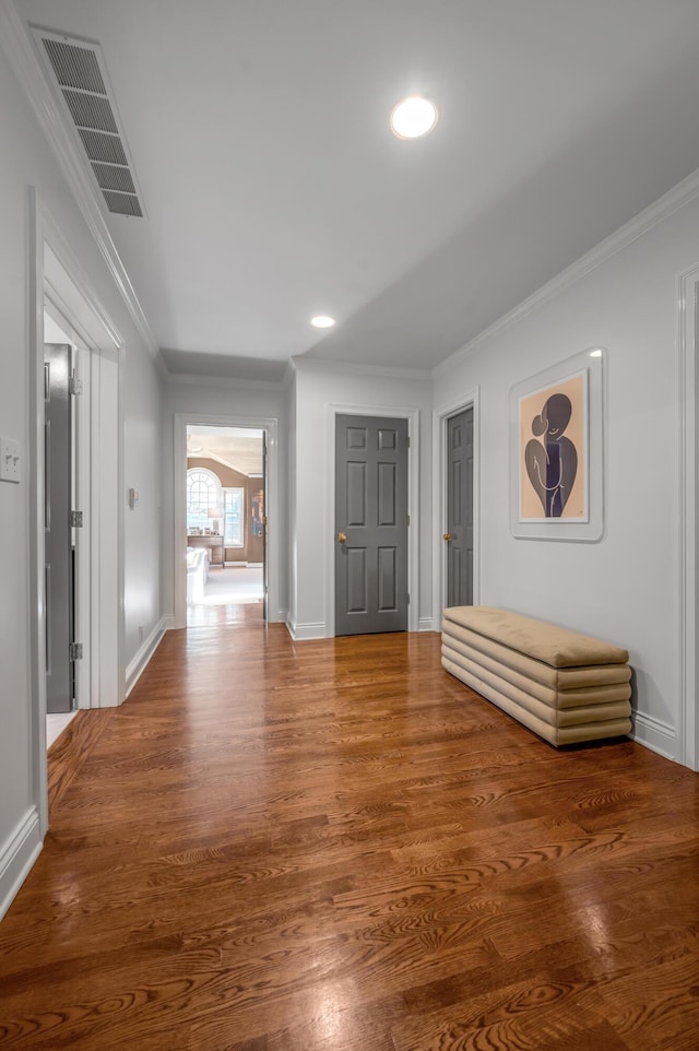 corridor featuring crown molding, wood finished floors, baseboards, visible vents, and recessed lighting